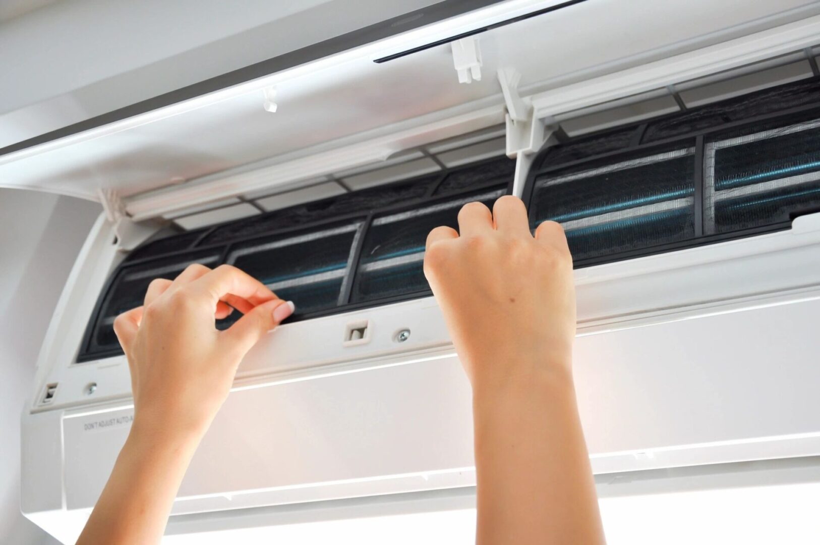 Hands installing or cleaning an air conditioner filter.