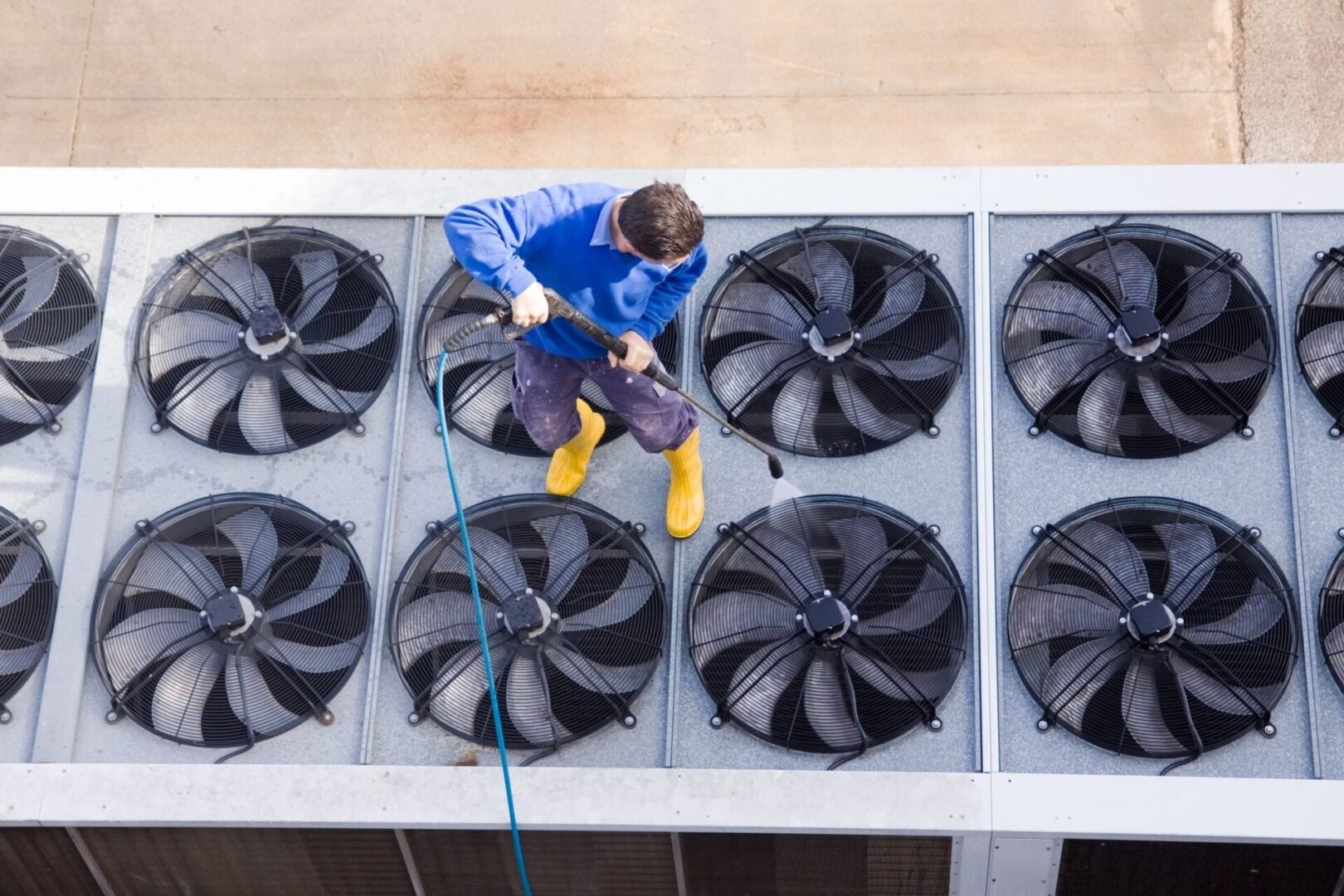 Person cleaning large industrial cooling fans with a hose.