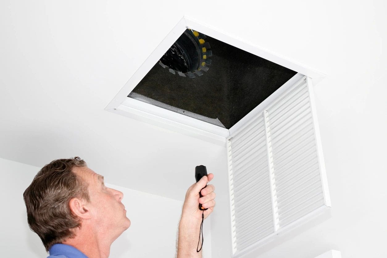 Man inspecting attic with flashlight through ceiling hatch.
